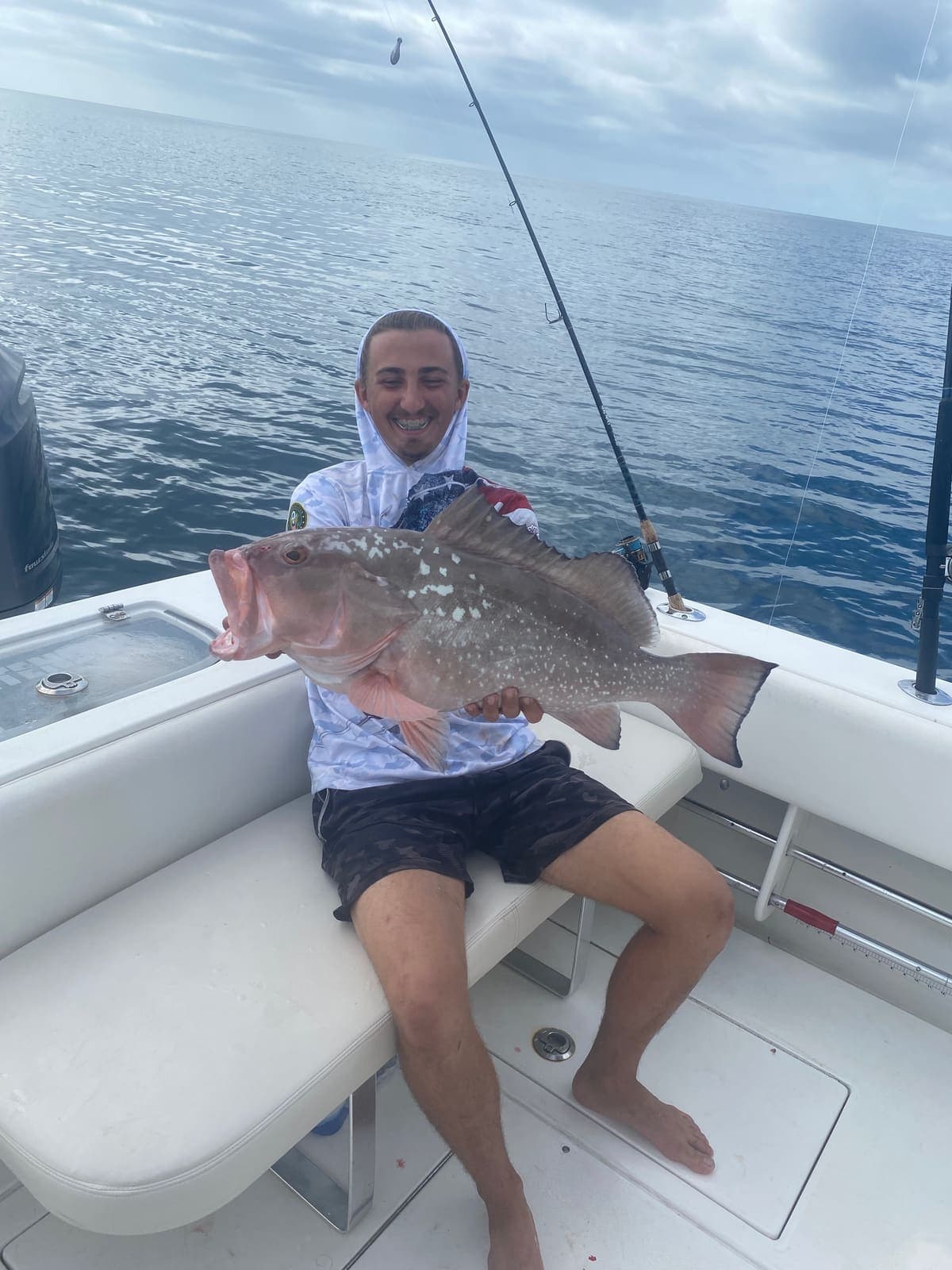 Guest smiling with a large red grouper aboard the boat